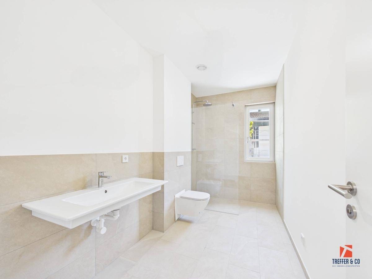 Modernes Badezimmer mit großem Waschbecken, wandhängendem WC und ebenerdiger Dusche.