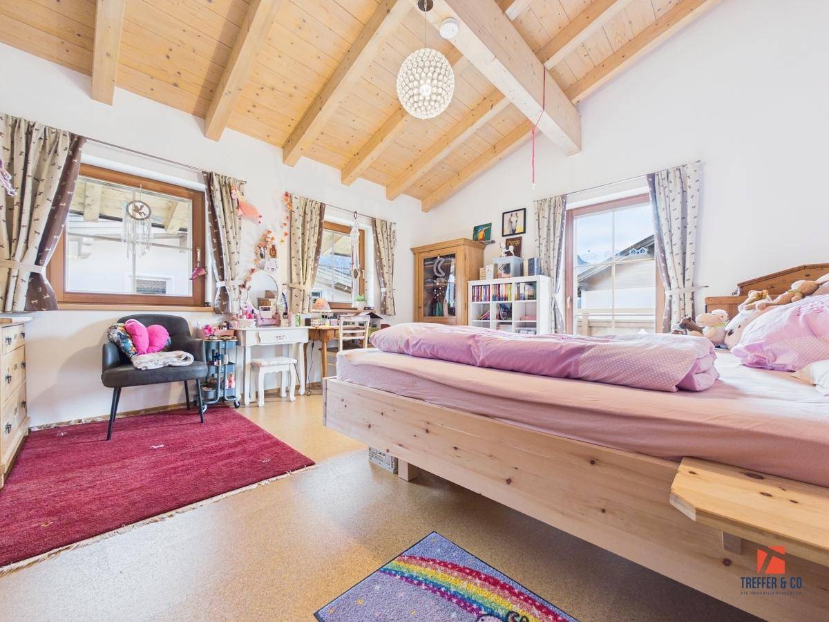 Helles Kinderzimmer mit Holzbalkendecke, großem Bett und Fenstern, die viel Licht hereinlassen.
