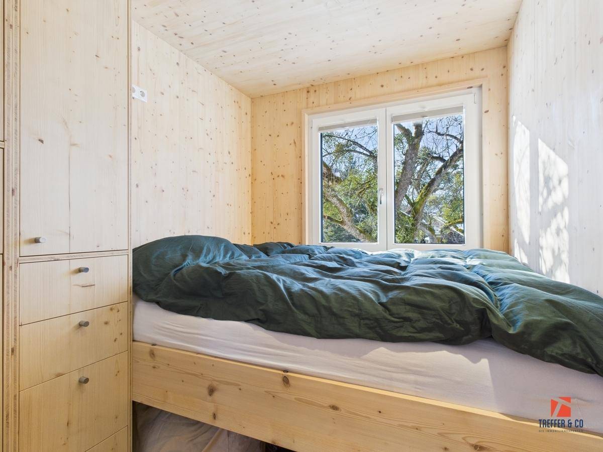 Kleines Schlafzimmer mit Holzwänden, integriertem Bett und Schränken sowie Blick ins Grüne.