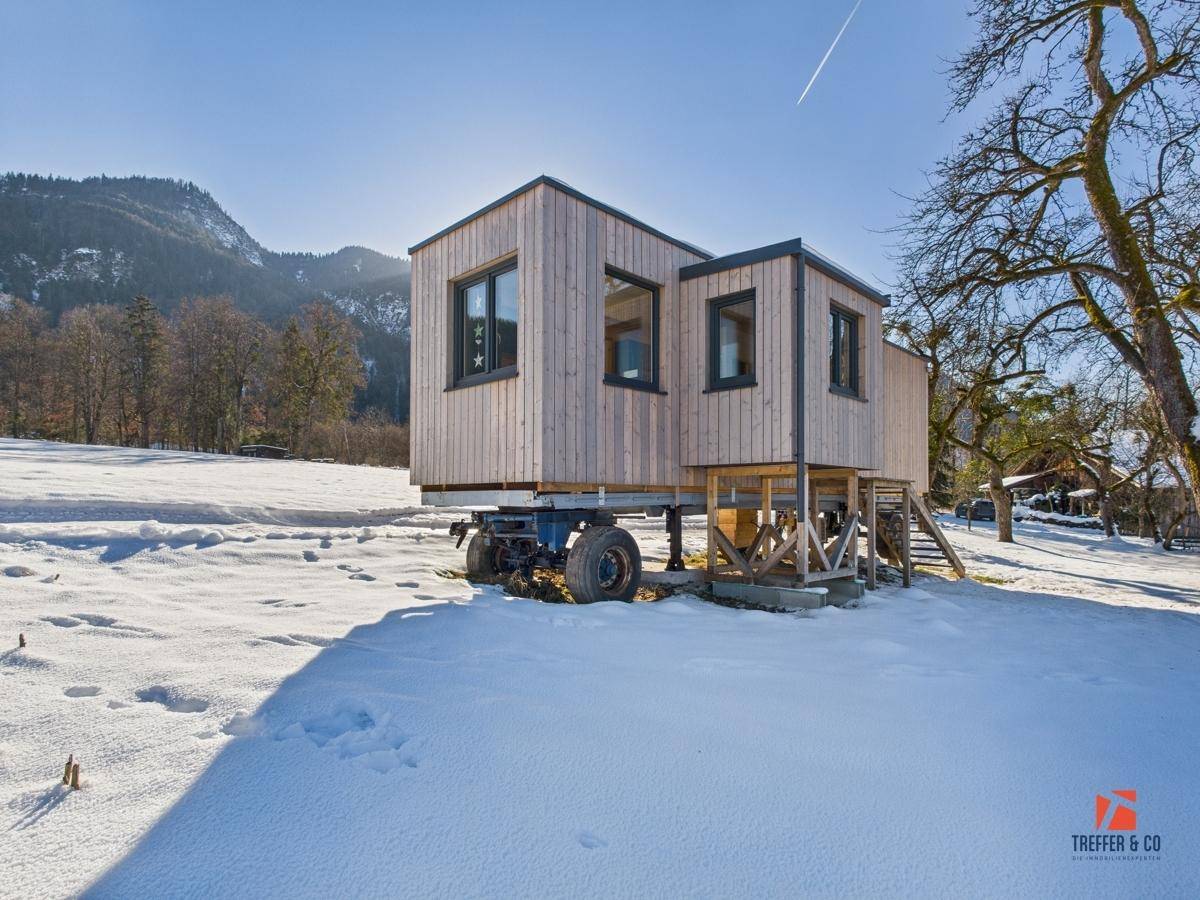 Modulares Tiny House auf Rädern in einer sonnigen, verschneiten Landschaft mit Bergen im Hintergrund.