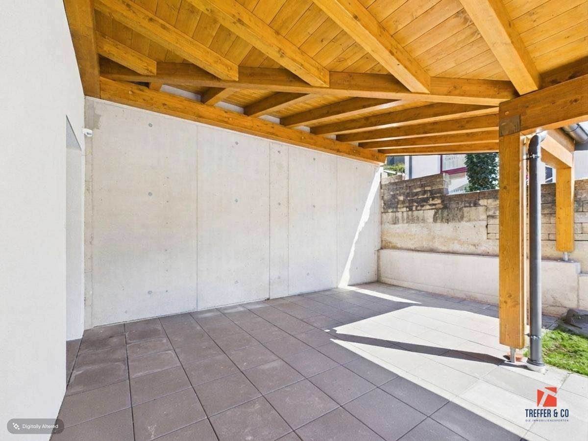 Geräumige überdachte Terrasse mit Fliesenboden und sichtbaren Holzbalken.