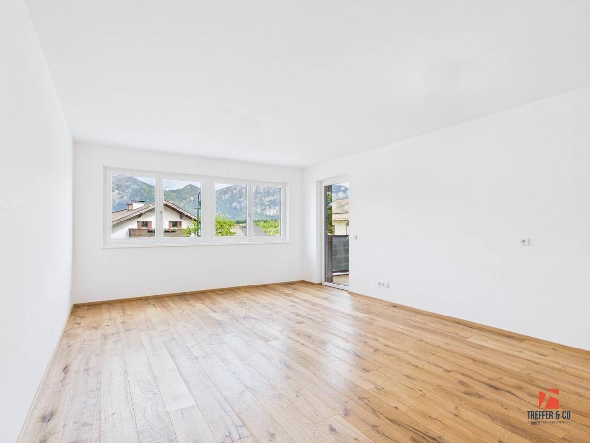 Heller Wohnraum mit Holzboden, großen Fenstern und Zugang zu einem Außenbereich.