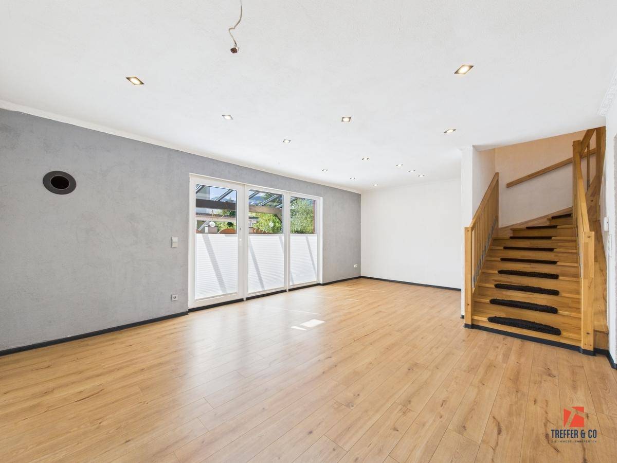 Helles Wohnzimmer mit Laminatboden, grauer Akzentwand und Blick ins Grüne.