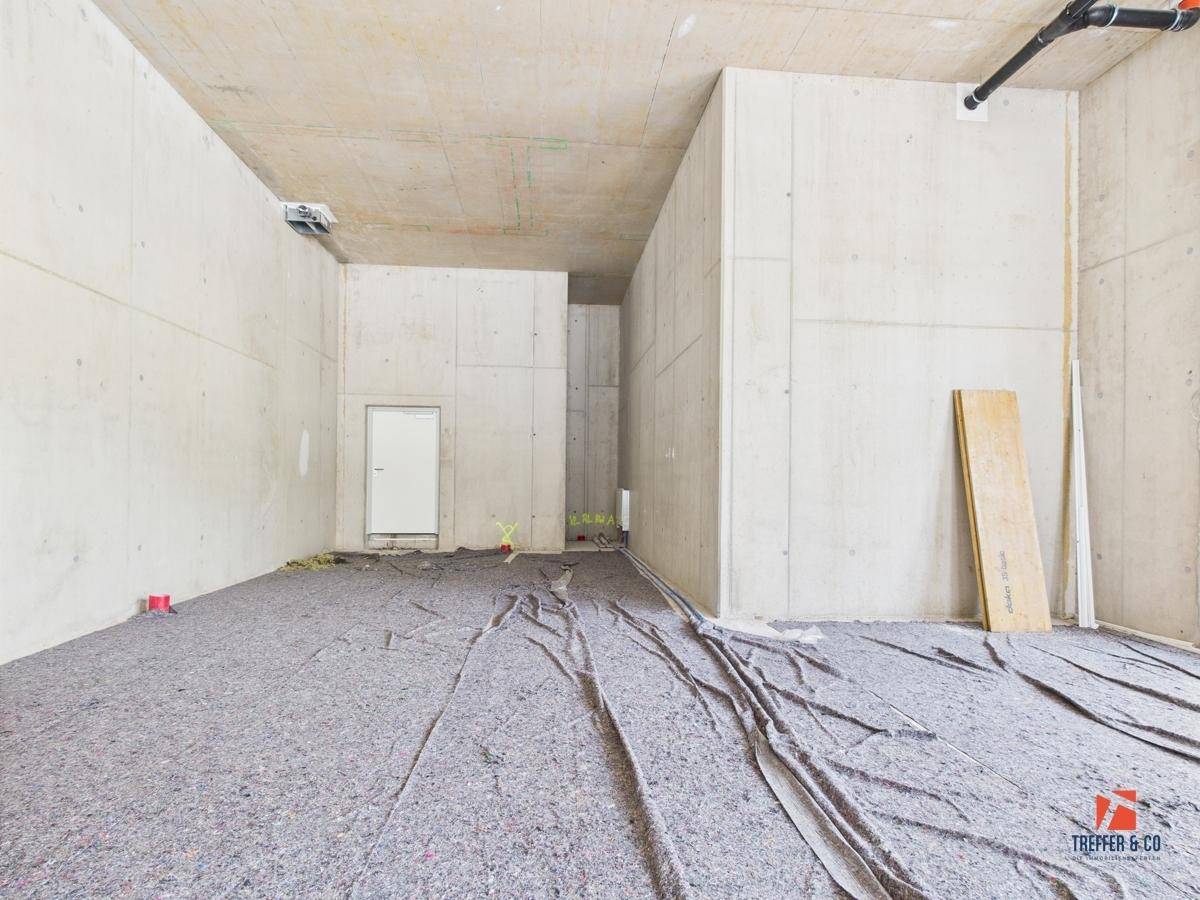 Großer Gewerberaum im Rohbau mit Betonwänden und -decke, vorbereitet für den weiteren Ausbau.