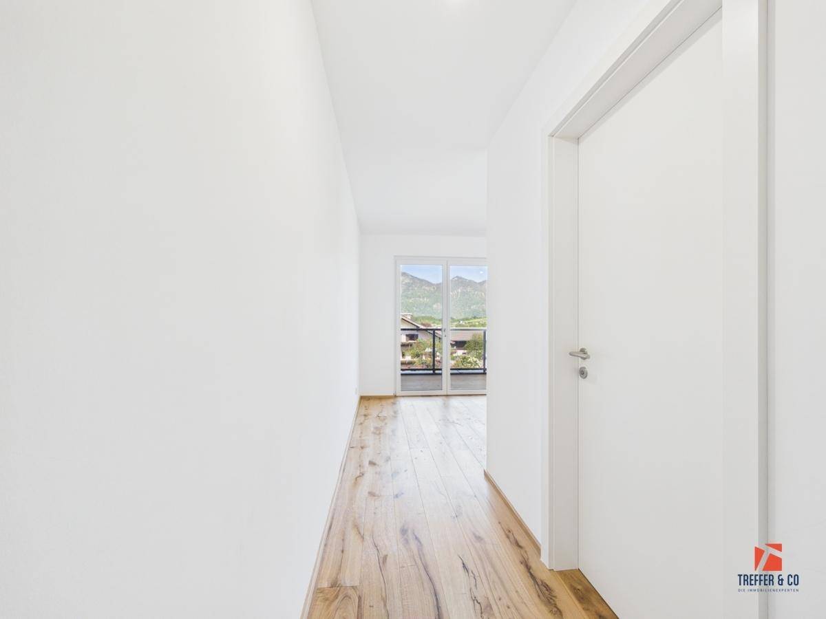 Heller Flur mit Holzboden, der zu einem Raum mit Balkon und Bergblick führt.
