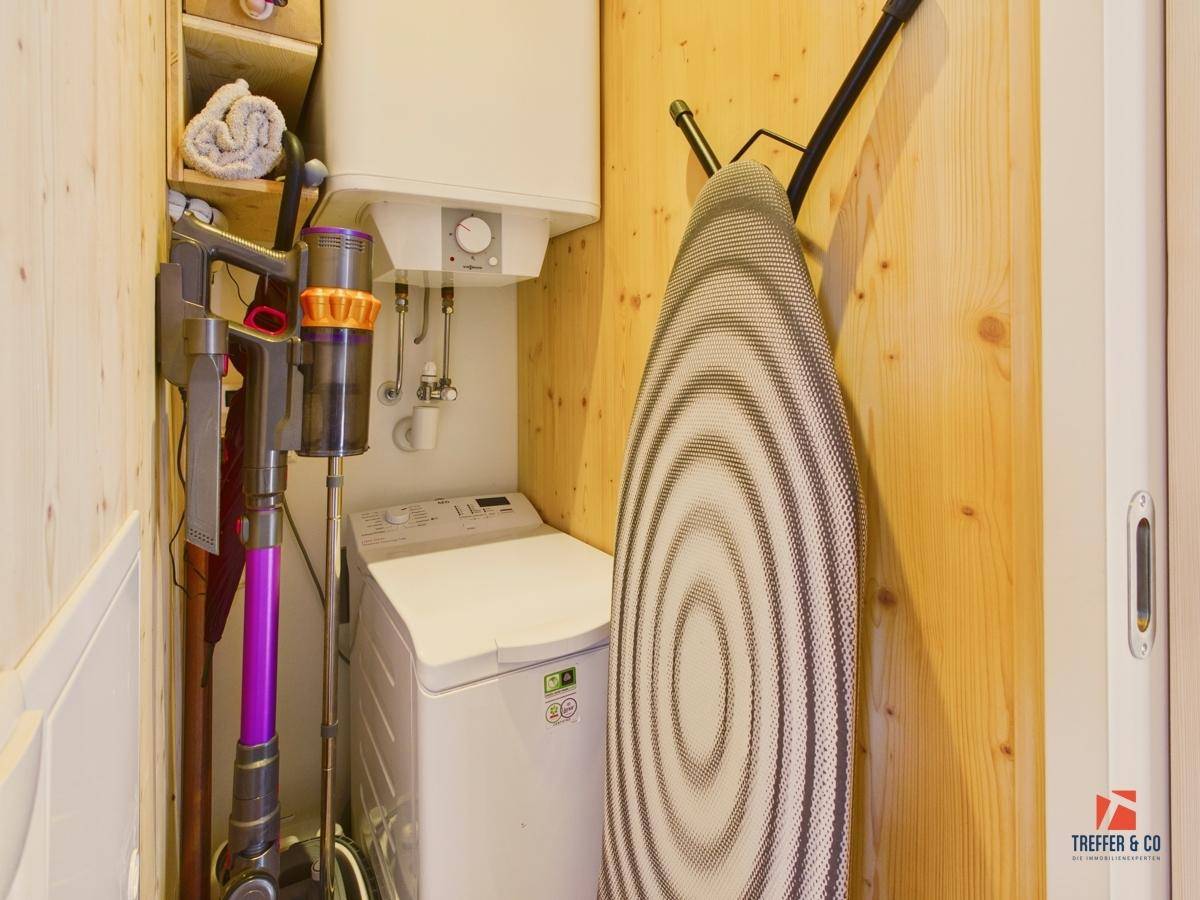 Praktischer Hauswirtschaftsraum mit Staubsauger, Bügelbrett und Holzverkleidung.