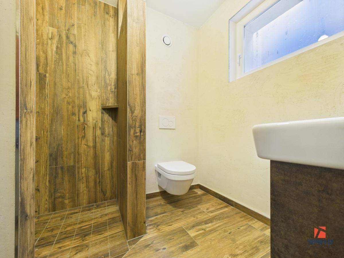 Badezimmer mit Holzoptik-Fliesen, wandhängendem WC, Waschtisch und kleinem Fenster.