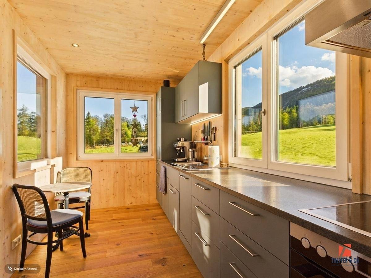 Helle Küche mit Holzverkleidung, grauen Unterschränken und Essbereich mit Blick ins Grüne.