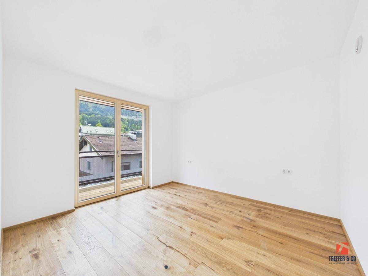 Helles Schlafzimmer mit Holzboden und großen Fenstern, die viel Tageslicht hereinlassen.