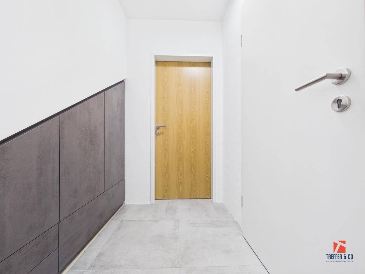 Moderner Flur mit Fliesenboden, integriertem Stauraum und zwei Holztüren.