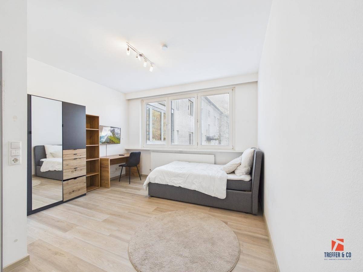 Modern eingerichtetes Schlafzimmer mit Einzelbett, Schreibtisch, Kleiderschrank und einem runden Teppich.