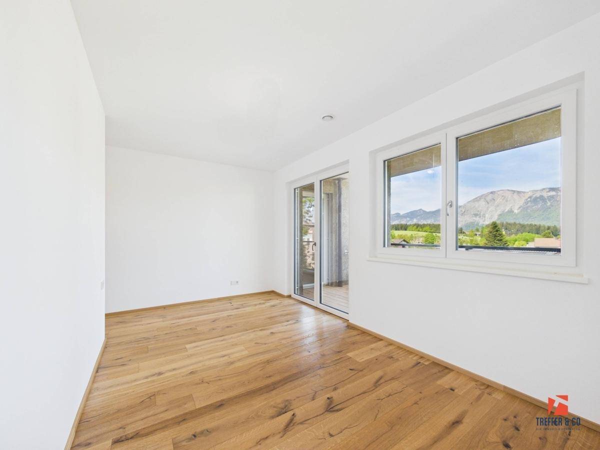 Geräumiges Schlafzimmer mit Holzboden, Balkonzugang und Panoramablick auf die Berge.