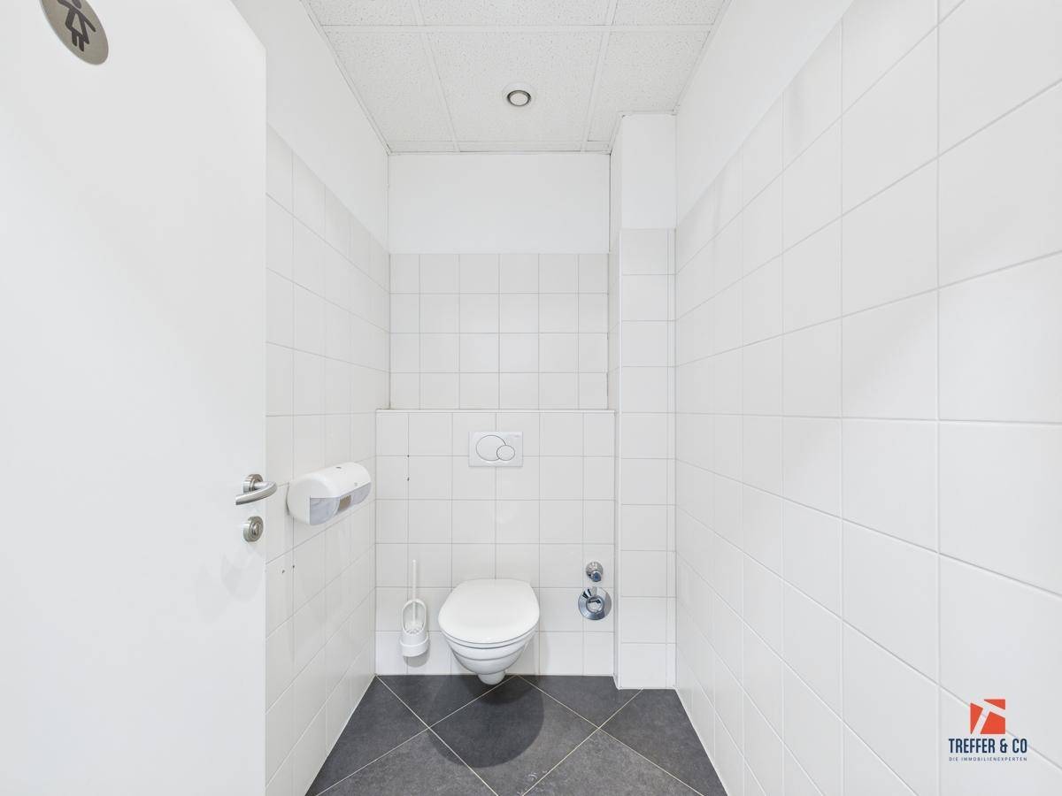 Helle und gepflegte Toilette mit Wand-WC und weißen Fliesen an den Wänden.