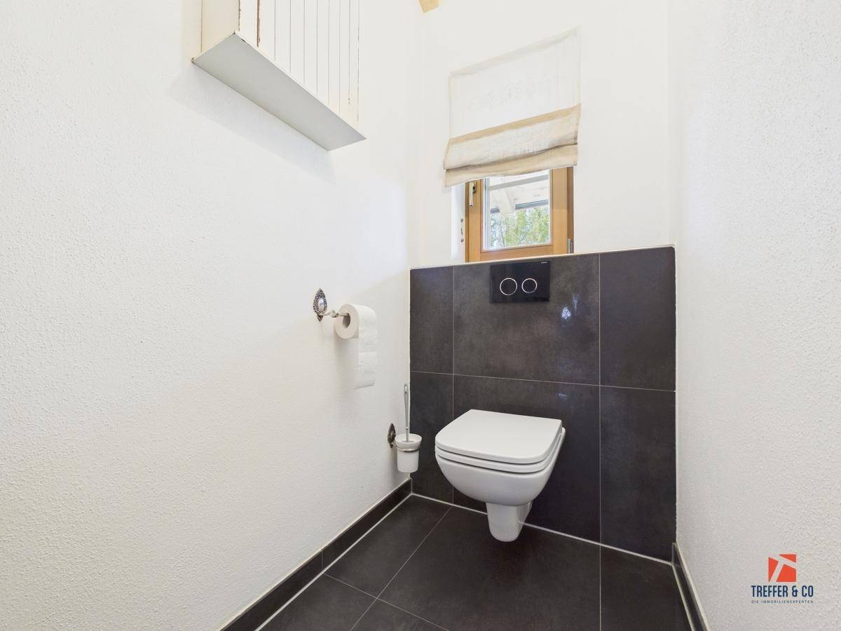 Modernes Gäste-WC mit dunklen Fliesen, wandhängender Toilette und einem kleinen Fenster.