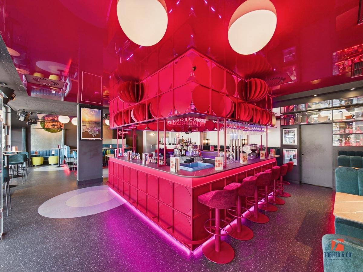 Auffällige pinke Bartheke mit integrierter Beleuchtung und modernem Design im Zentrum des Raumes.