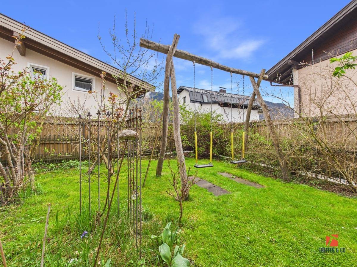 Grüner Gartenbereich mit einer rustikalen Holzschaukel und viel Platz für Kinder zum Spielen.