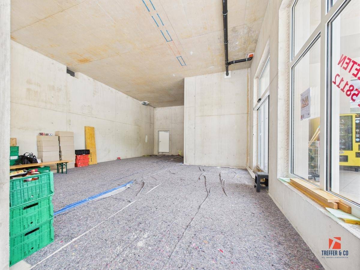 Geräumiger Gewerberaum im Rohbau mit einigen gelagerten Gegenständen und Blick ins Grüne.