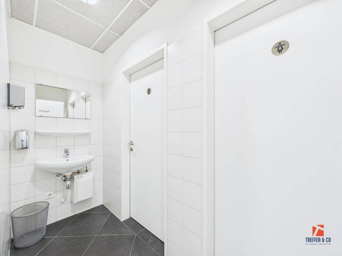 Heller und sauberer Sanitärbereich mit Waschbecken, Spiegel und zwei separaten Toilettenkabinen.