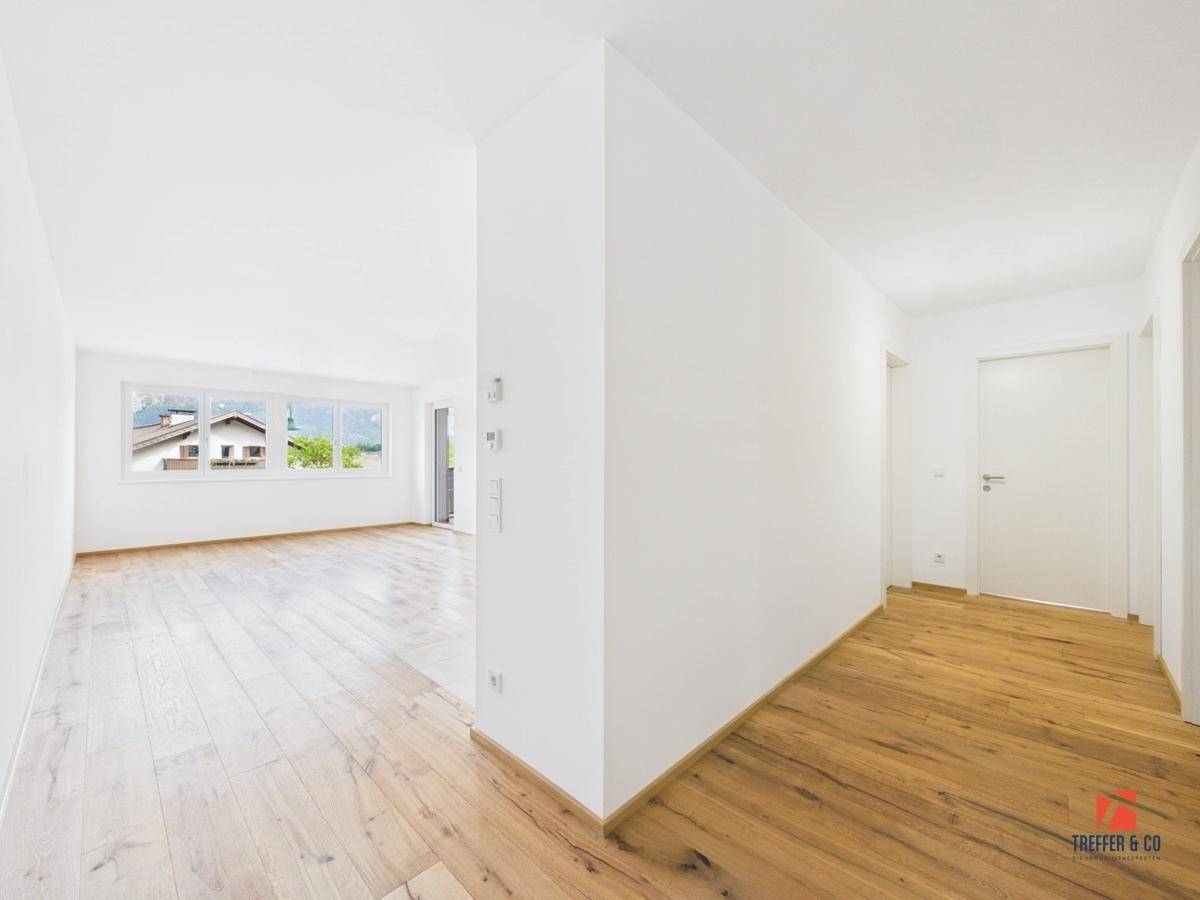 Geräumiger Wohnbereich mit Holzboden und großen Fenstern, die viel Licht hereinlassen.