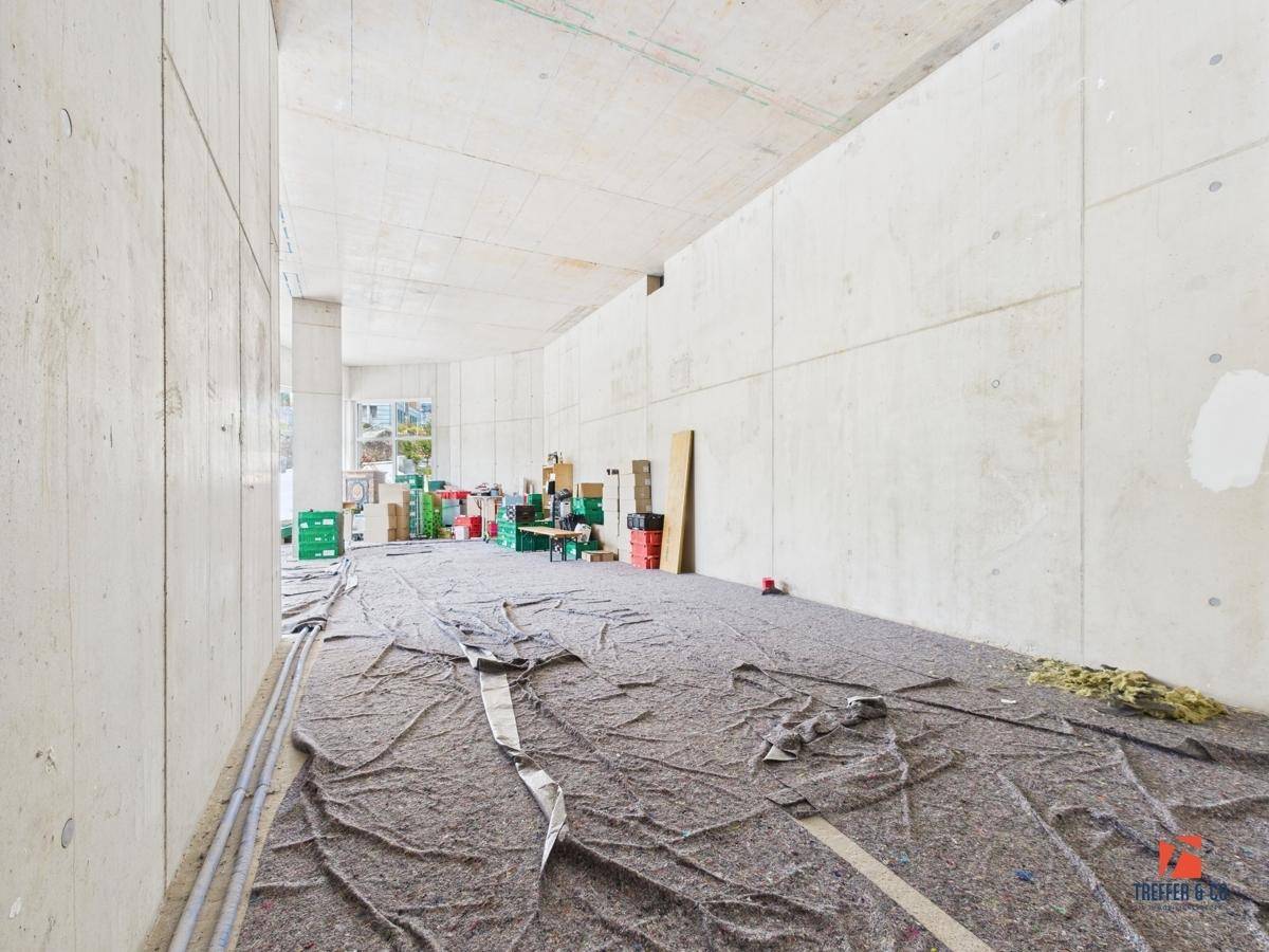 Geräumiger Gewerberaum im Rohbau mit großen Fenstern und Blick auf die grüne Umgebung.