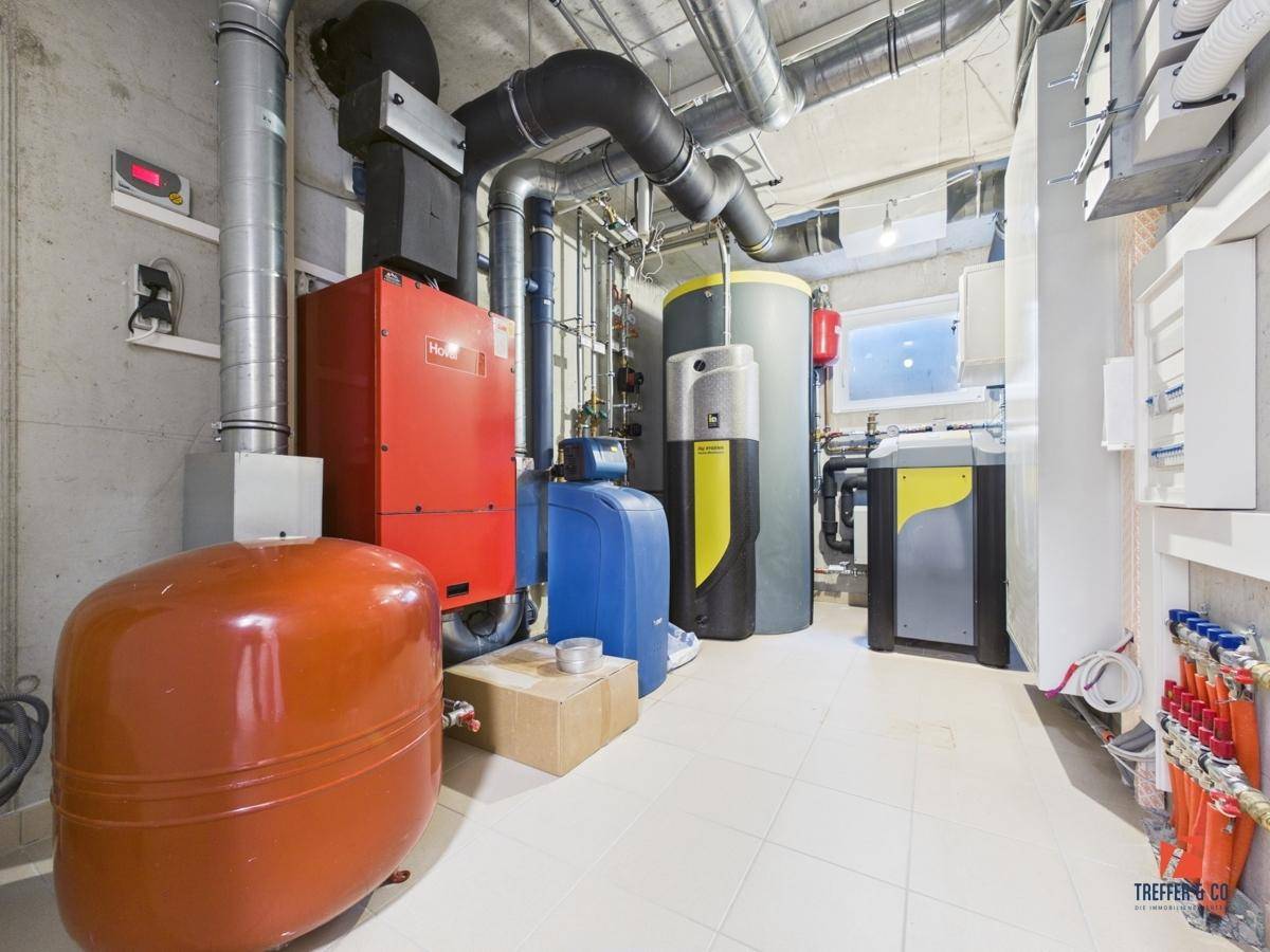 Moderner Technikraum im Keller mit Heizungs- und Lüftungsanlagen sowie sichtbaren Rohren und Leitungen.