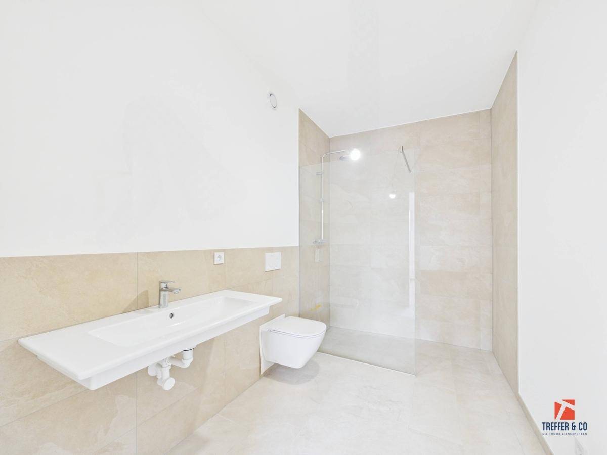Modernes Badezimmer mit beigefarbenen Fliesen, großer Dusche und wandhängendem WC.