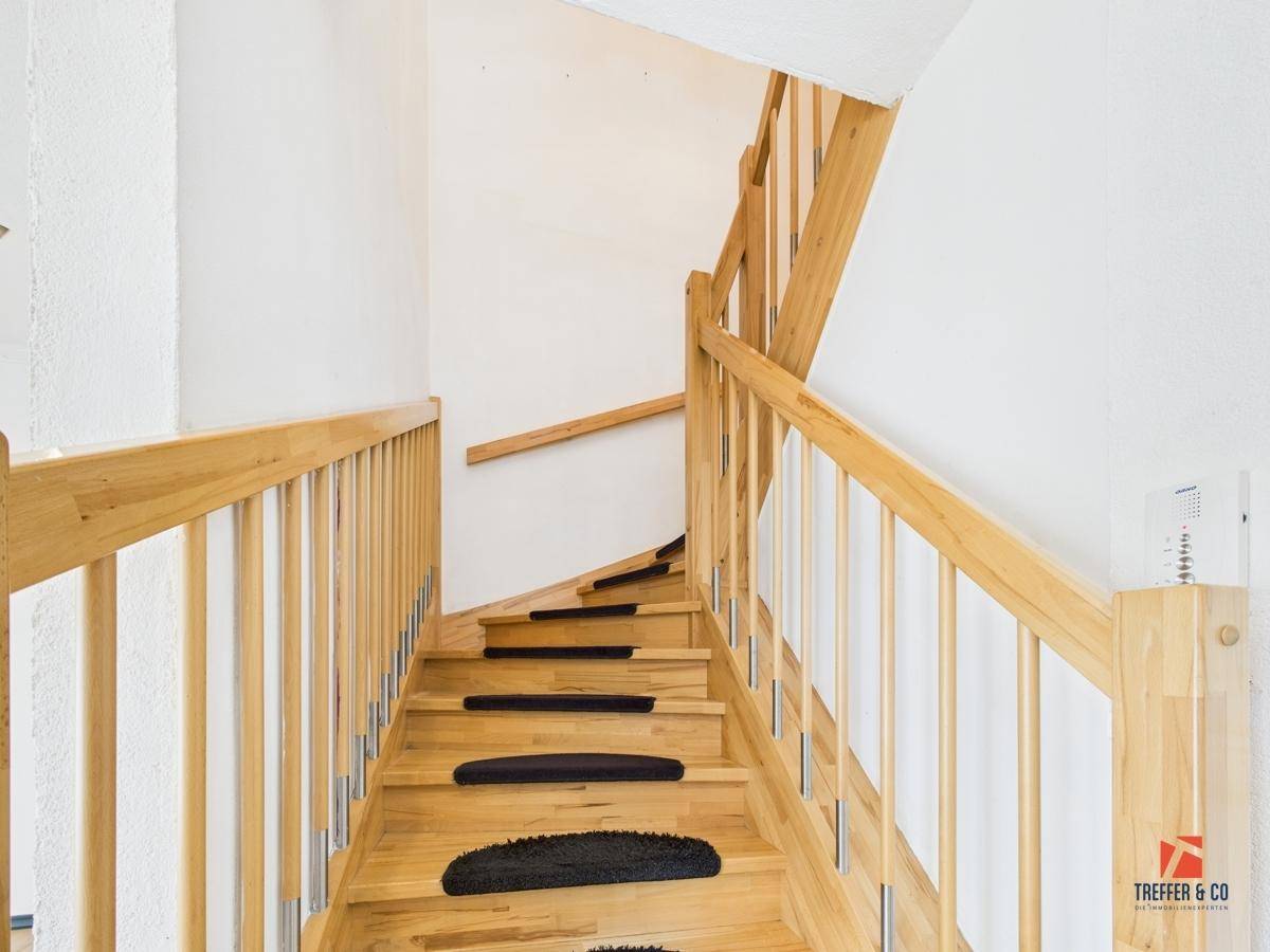 Holztreppe mit Teppichstufen und hellem Geländer, die in die obere Etage führt.