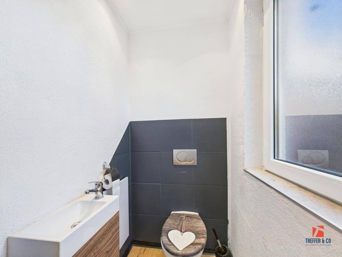 Modernes Gäste-WC mit Wand-WC, kleinem Waschbecken und Fenster für Tageslicht.