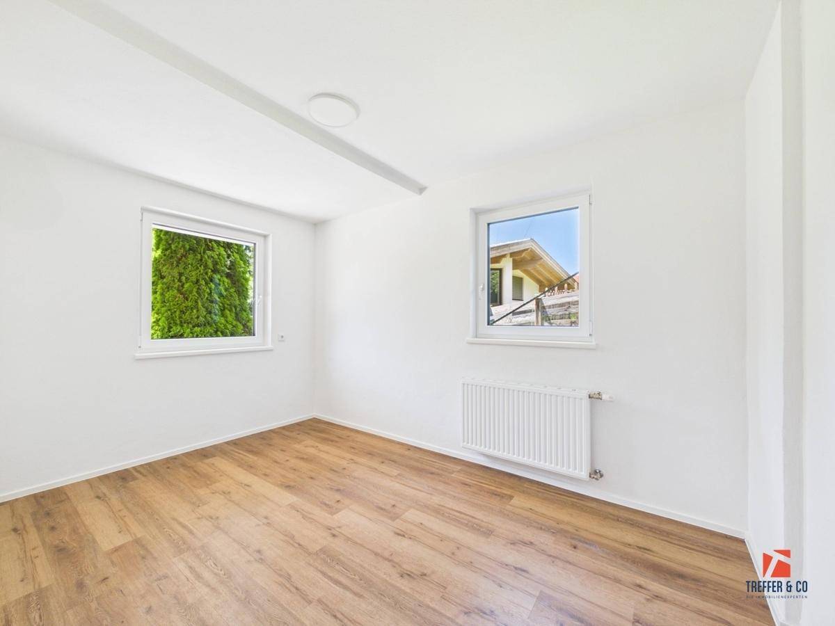 Helles Zimmer mit Holzboden und zwei Fenstern, die viel Tageslicht hereinlassen.
