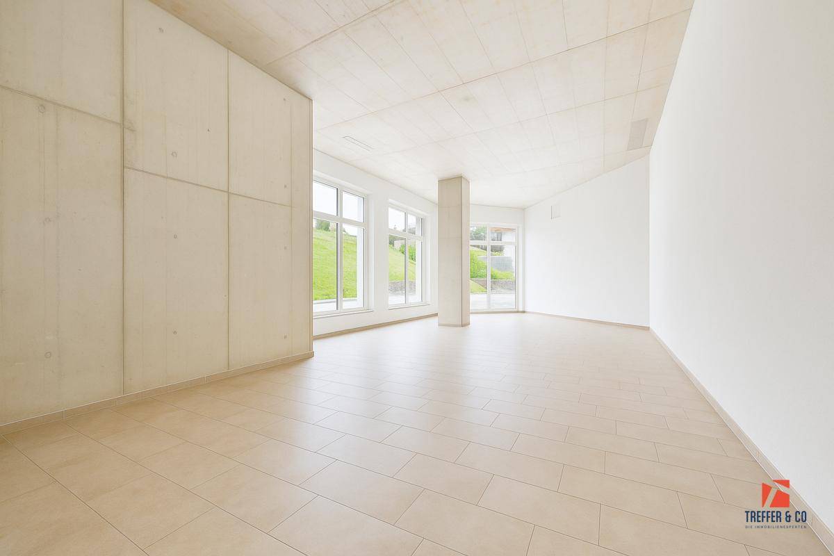 Geräumiger, leerer Gewerberaum mit großen Fenstern, Fliesenboden und Betonwänden.