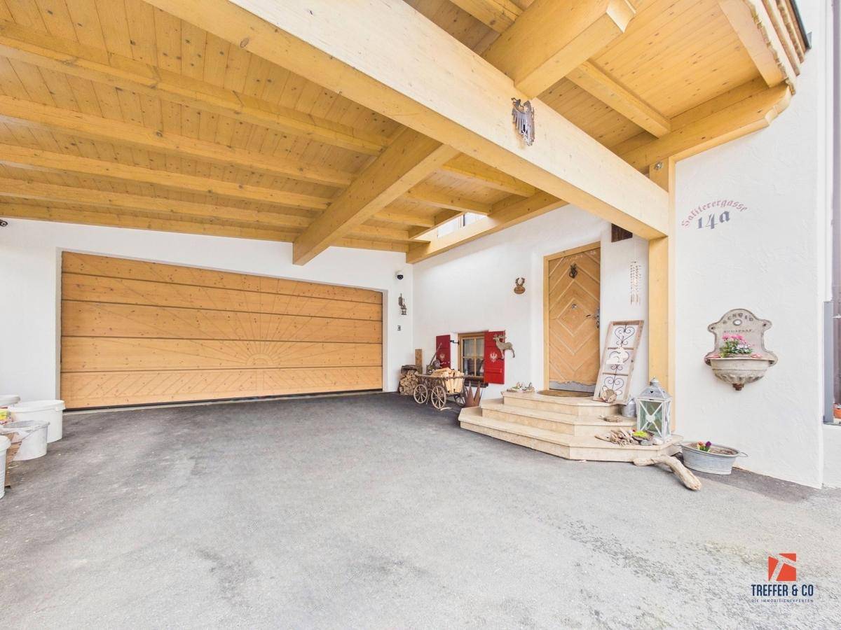 Überdachter Eingangsbereich mit sichtbaren Holzbalken, großer Garagentür und alpinen Dekorationen.