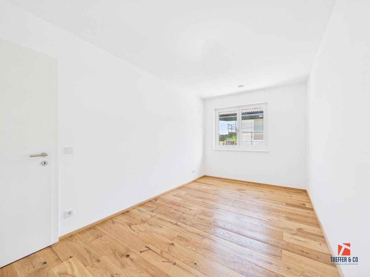 Helles, leeres Zimmer mit Holzboden und Fenster, ideal als Schlaf- oder Arbeitszimmer.