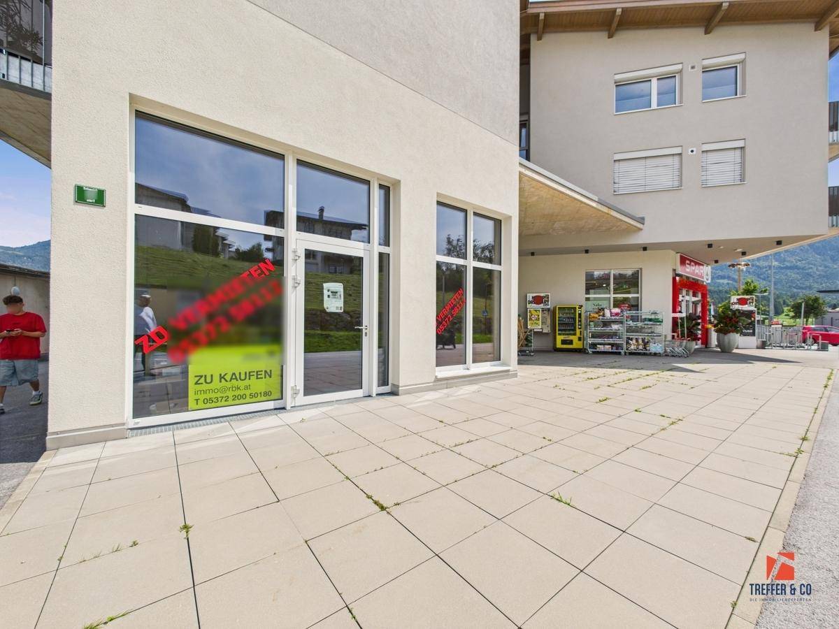 Erdgeschossfassade eines Geschäftsgebäudes mit großen Schaufenstern und gepflastertem Zugangsbereich.