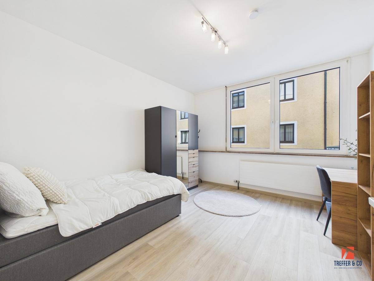 Helles Schlafzimmer mit Einzelbett, Kleiderschrank mit Spiegeltür und einem Schreibtisch am Fenster.