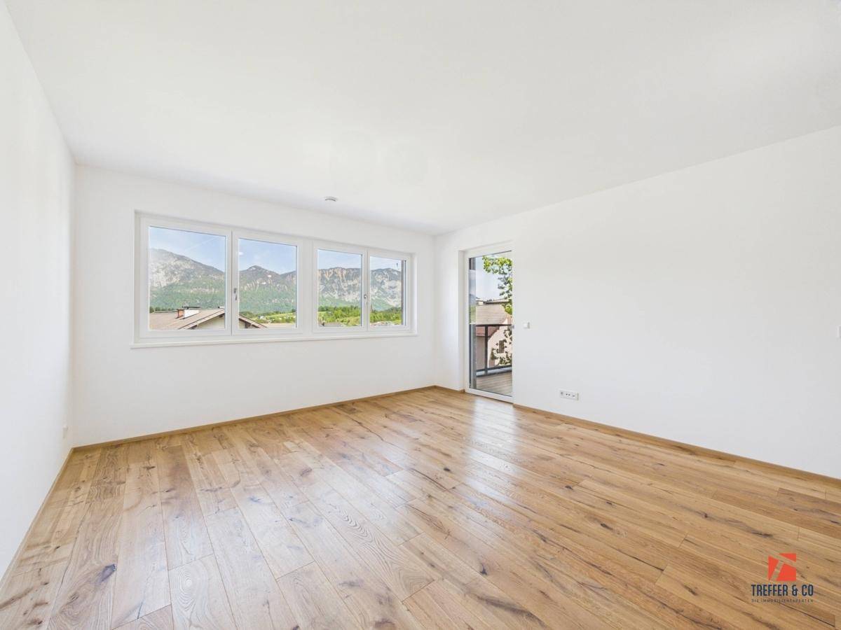 Helles Schlafzimmer mit Holzboden, Bergblick durch die Fenster und Balkonzugang.