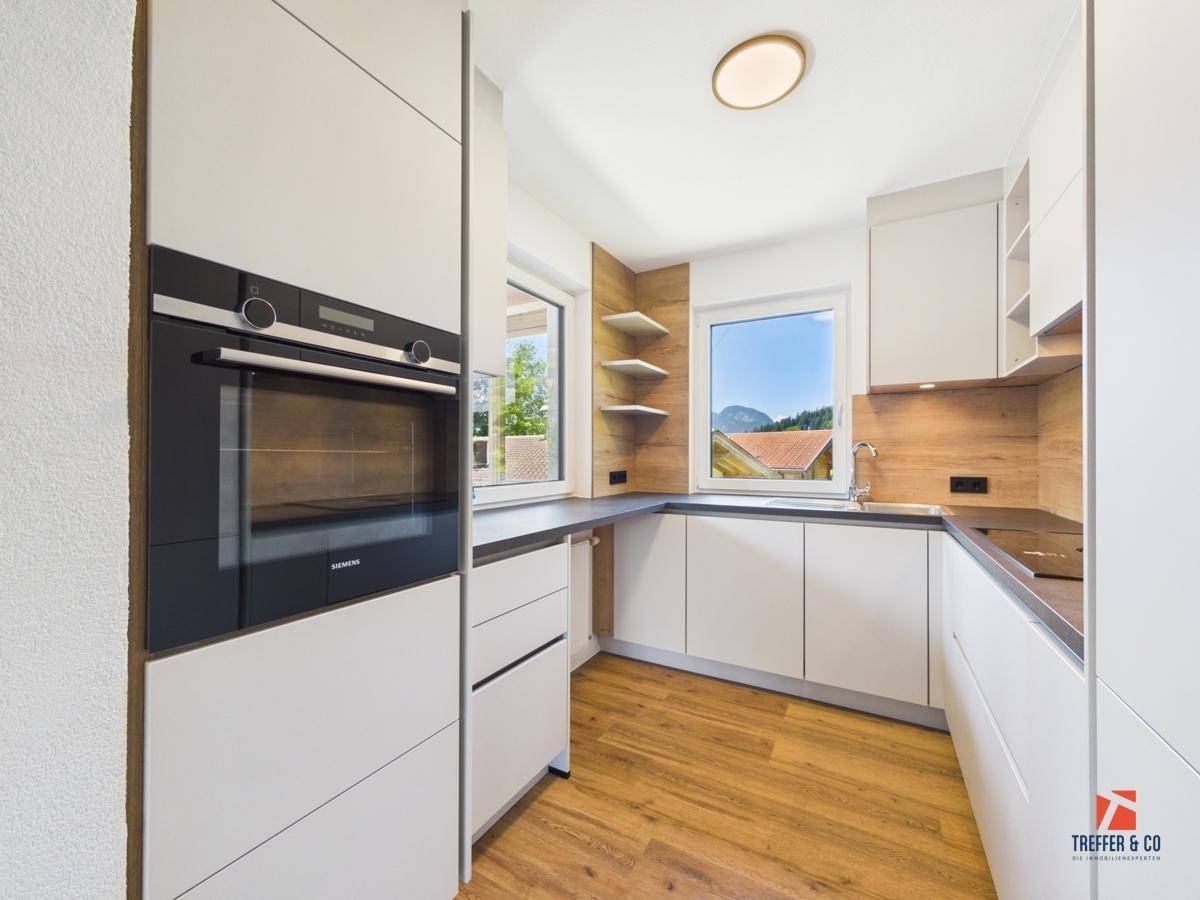 Moderne Küche mit weißen Schränken, integriertem Backofen und Blick ins Grüne.
