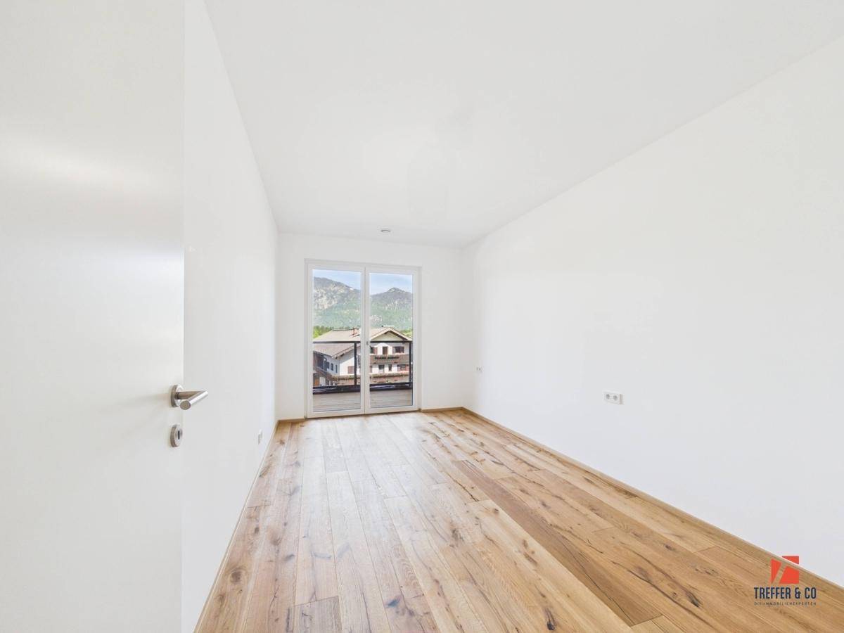 Geräumiges Schlafzimmer mit Holzboden und Balkonzugang, mit Blick auf die Umgebung.