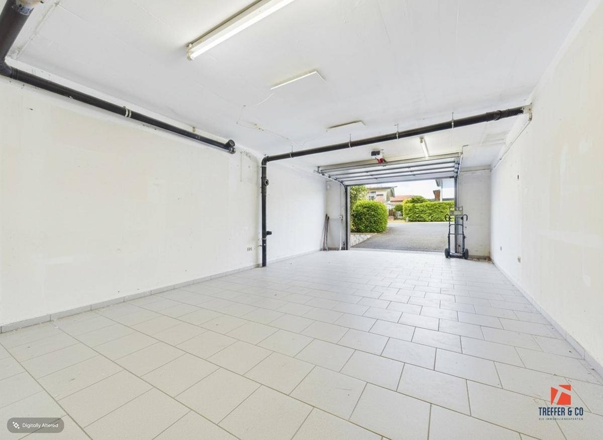 Helle Garage mit gefliestem Boden und offenem Tor, das den Blick auf die Einfahrt freigibt.