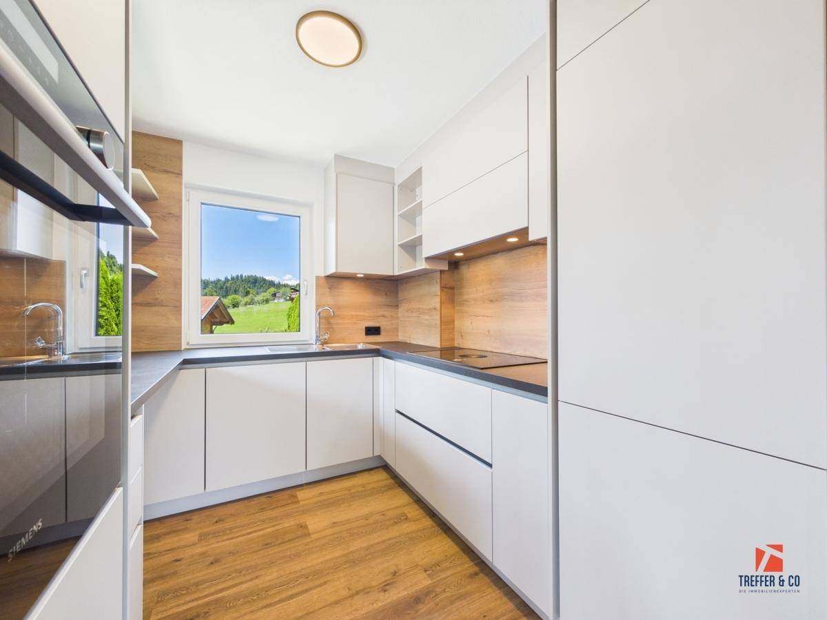 Helle, moderne Küche mit weißen Fronten, Holzakzenten und hochwertigen Geräten.