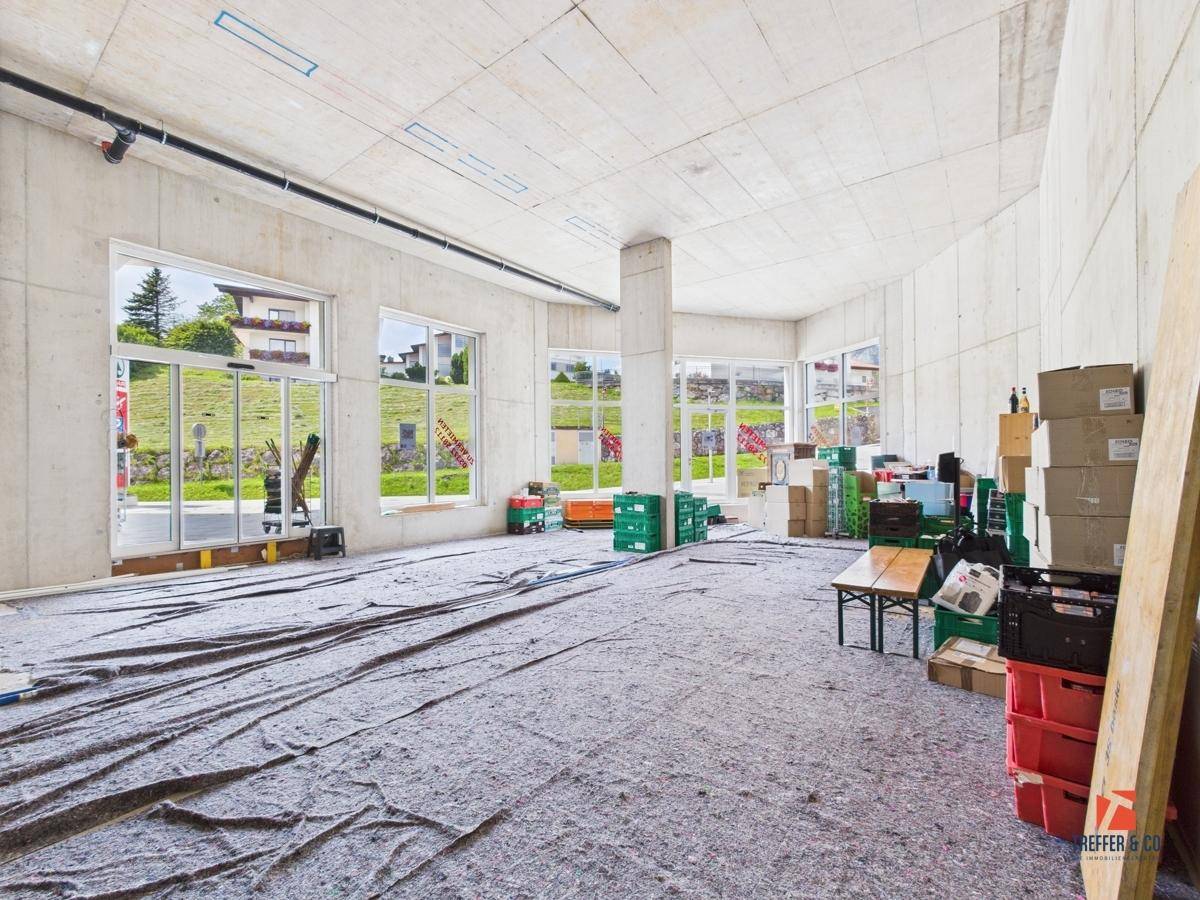 Geräumiger Gewerberaum im Rohbau mit großen Fenstern und Blick auf die grüne Umgebung.