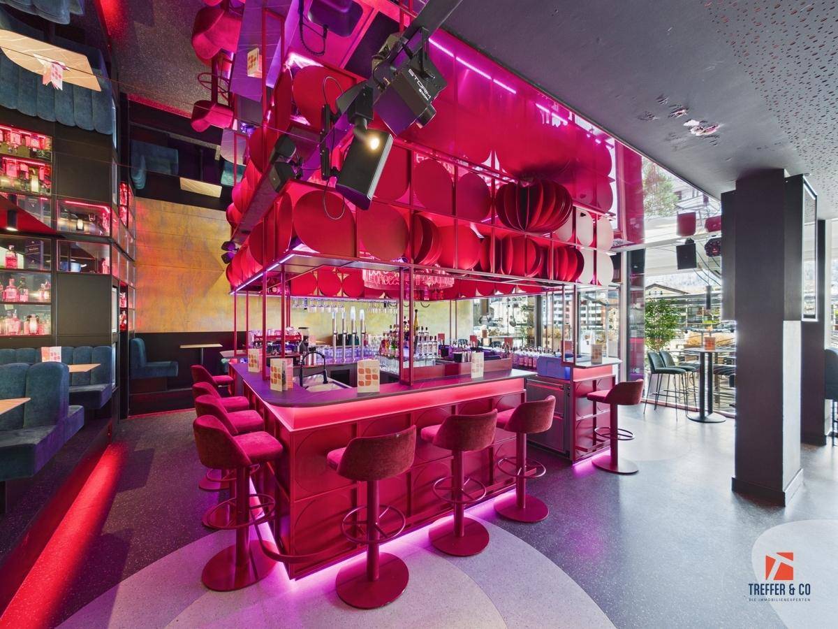 Moderner Barbereich mit leuchtend pinker Beleuchtung, Barhockern und einer gut bestückten Theke.