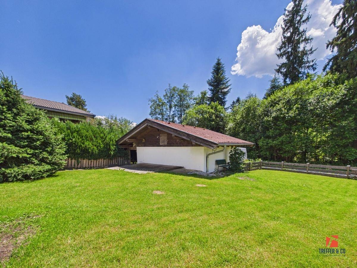 Weitläufiger Gartenbereich mit Rasen und einem Nebengebäude, umgeben von viel Grün.