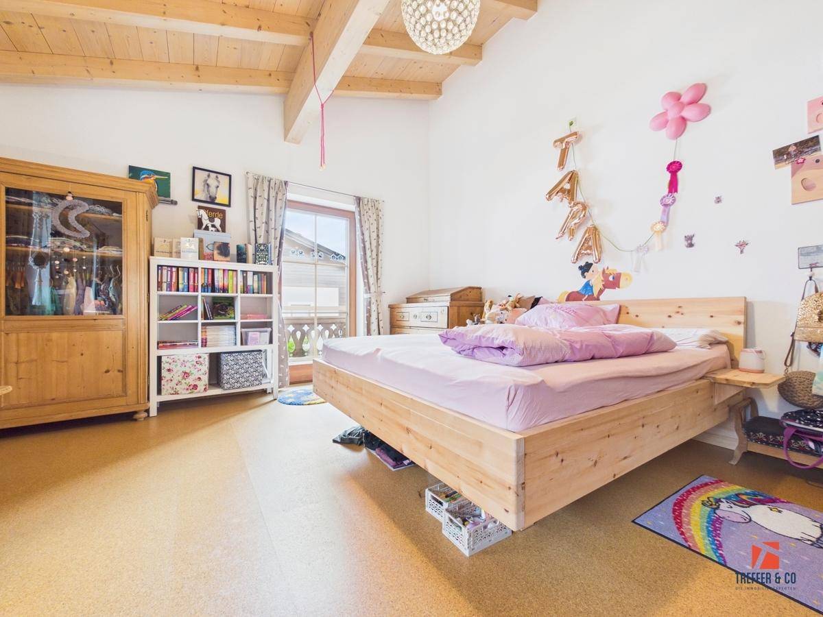 Kinderzimmer mit Holzbalkendecke, Holzbett und Zugang zu einem Balkon, hell und freundlich.