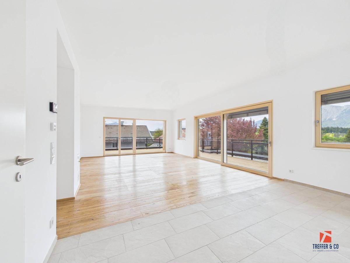Großer, heller Wohnraum mit Holzboden, Fliesenbereich und Zugang zu einem Balkon.