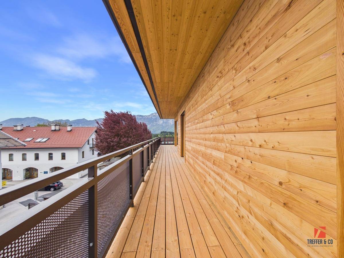 Langer Holzbalkon mit Metallgeländer und Blick auf die Stadt und die Berge.