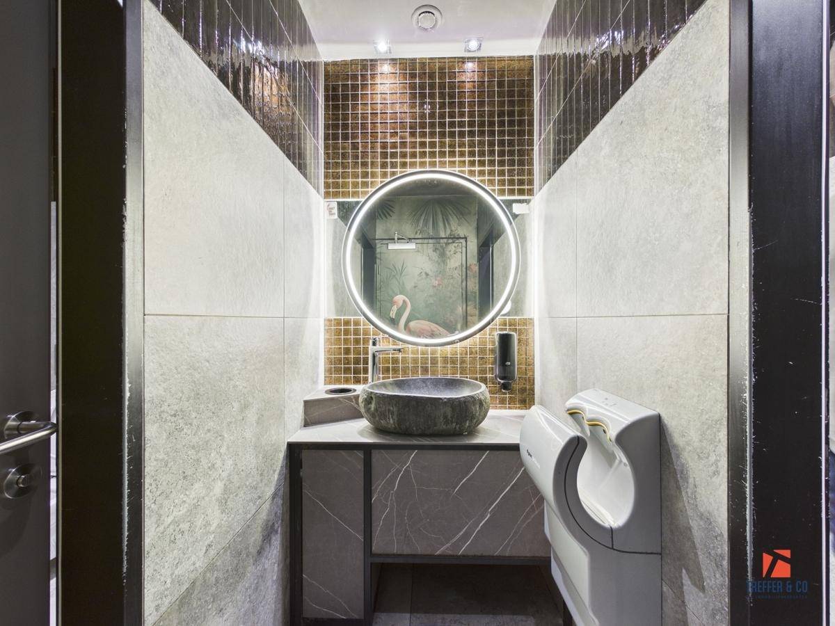 Modernes Badezimmer mit rundem Spiegel, goldenen Mosaikfliesen und einem Steinwaschbecken.