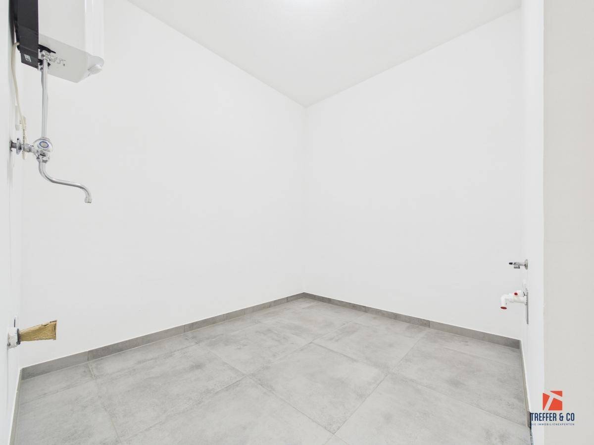 Praktischer Hauswirtschaftsraum mit Fliesenboden und Anschlüssen für Waschmaschine oder Spüle.