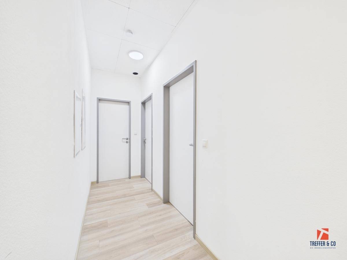 Heller Flur mit mehreren Türen und modernem Laminatboden, der zu verschiedenen Räumen führt.