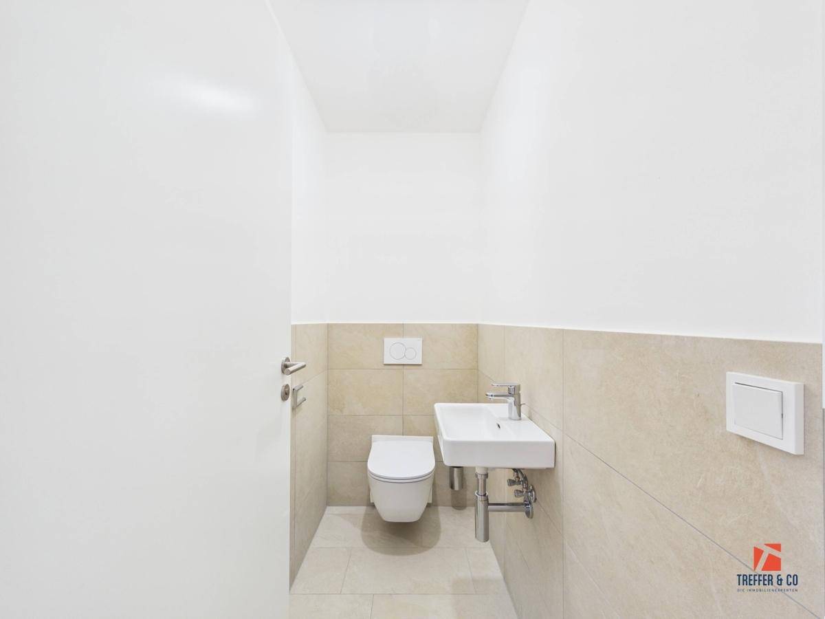 Separates Gäste-WC mit Wand-WC, kleinem Waschbecken und hellen Fliesen.