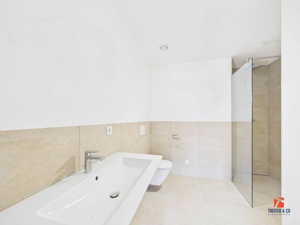Modernes Badezimmer mit großem Waschbecken, Duschbereich und beigen Fliesen.